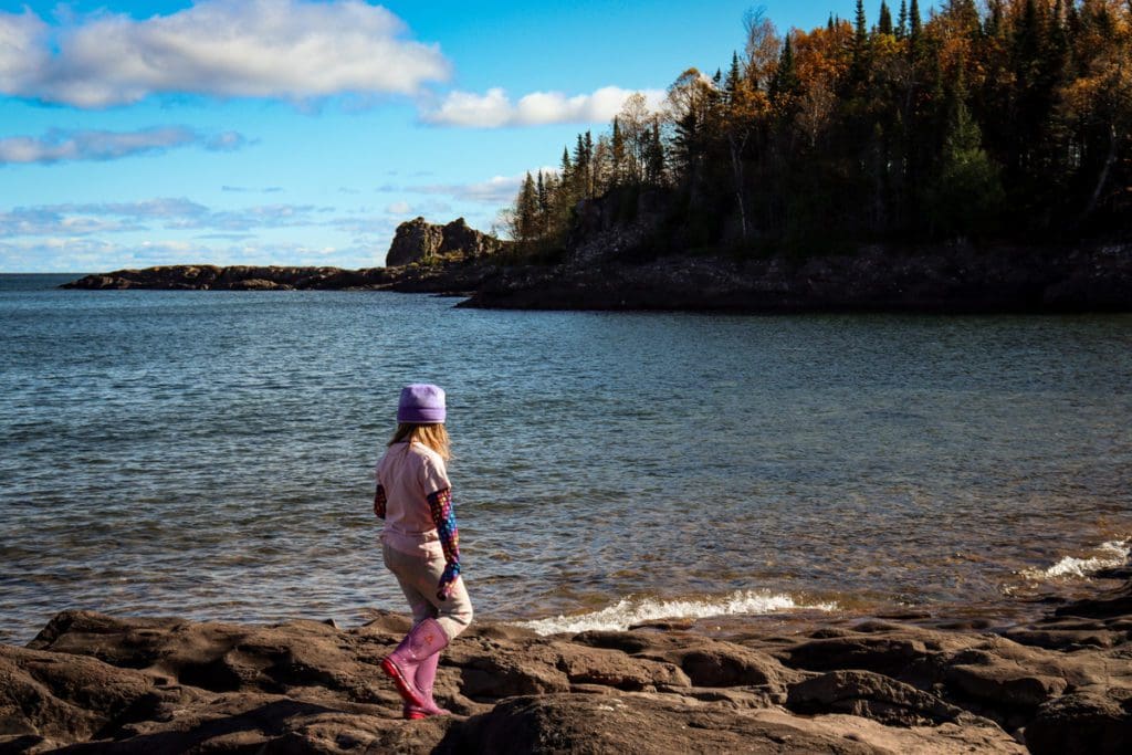 A young girl walks along the rocky beach, while hiking at Sugar Loaf Cove Nature Center, one of the best places to visit in northern Minnesota with kids.