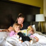 A mom and her young daughter read a book together, while snuggled up in bed at the Staybridge Suites in Eau Claire.
