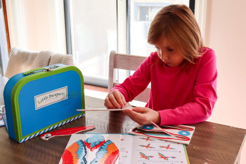 A young girl works on a macaw puppet activity from her Little Passports subscription box.