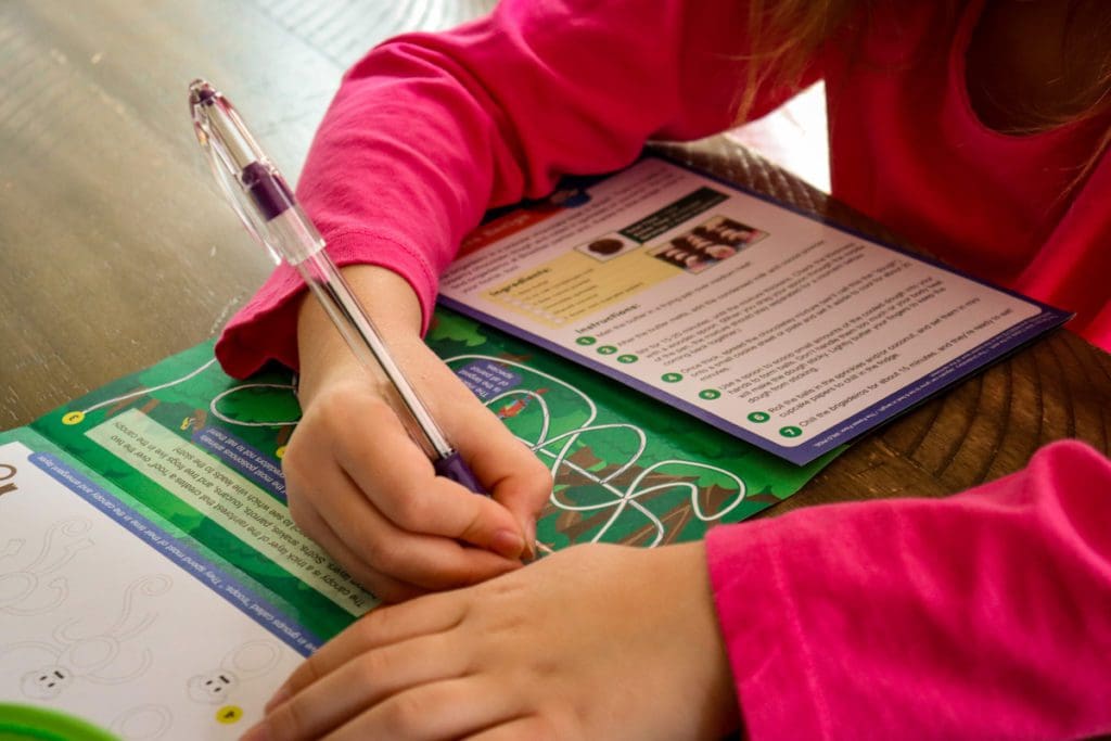 A young girl works on a maze activity in her Little Passports activity book.