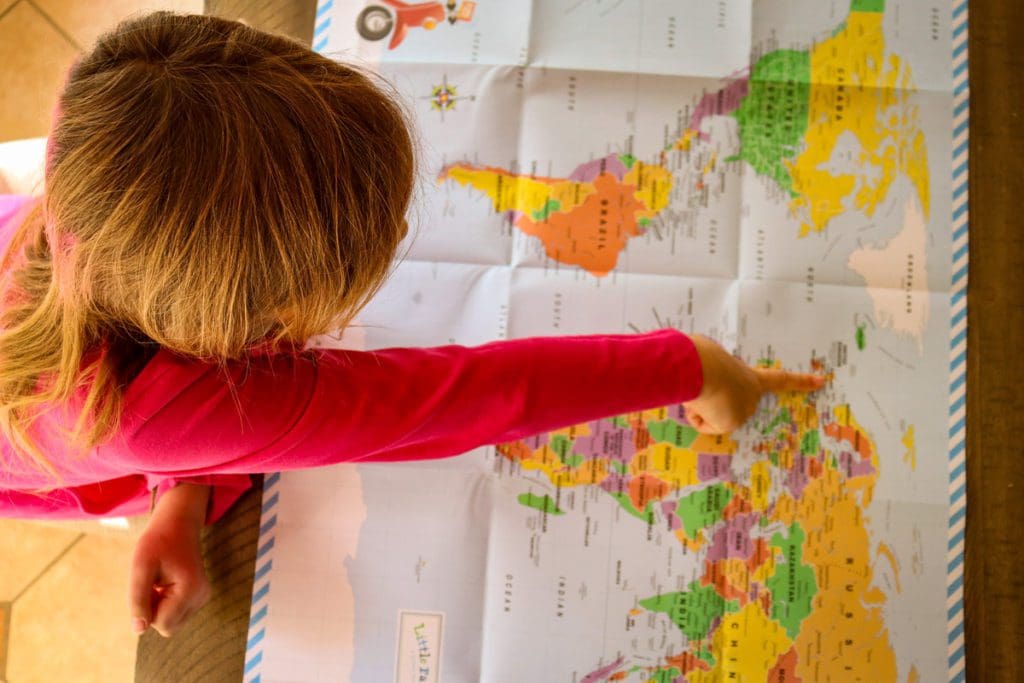 An overhead view of a little girl pointing to Europe on a map.