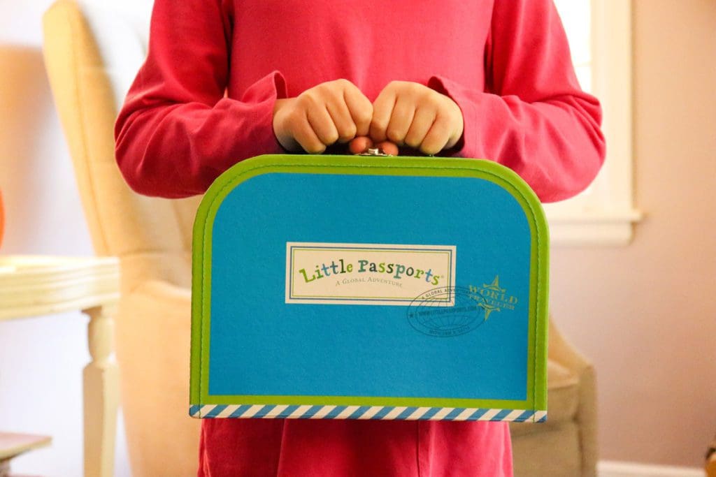 A close up of a little girl holding a Little Passports suitcase tight to her body.