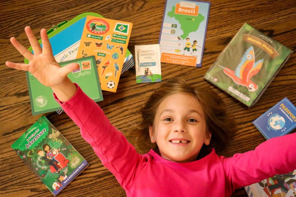 A young girl throws her hands in the air excitedly, with Little Passports activities surrounding her.