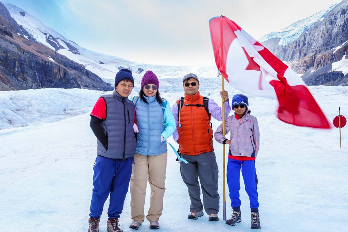 A family of four wearing winter gear and holding a large Canadian flag stand on the Columbia Icefield.