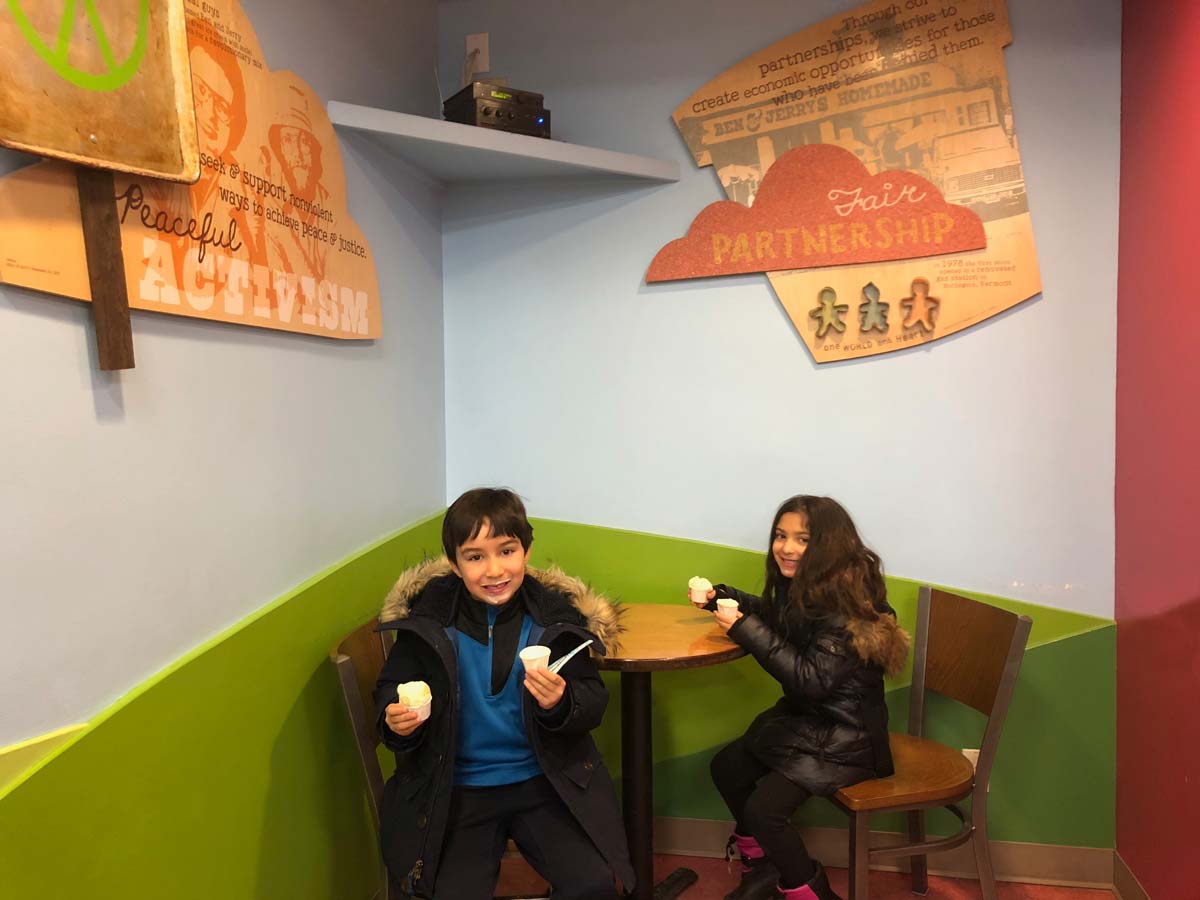 Two young kids eat ice cream at a small table while touring the Ben & Jerry’s Ice Cream Factory.