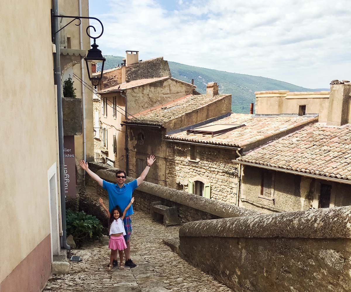 A young girl and her dad stand together with a rooftop view of Bonnieux behind them.