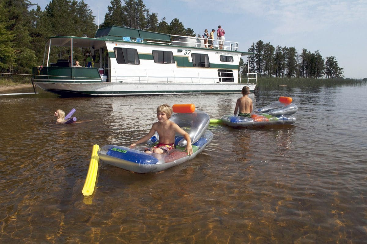 A family swims in front of their house boat, while exploring Rainy Lake in Voyageurs National Park, one of the best places to visit in northern Minnesota with kids.