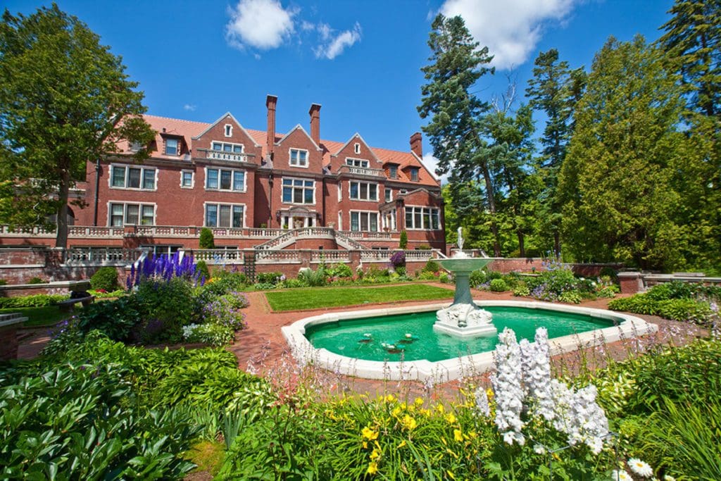 The rear exterior of Glensheen Mansion, featuring a fountain and lush grounds on a sunny day in Duluth.
