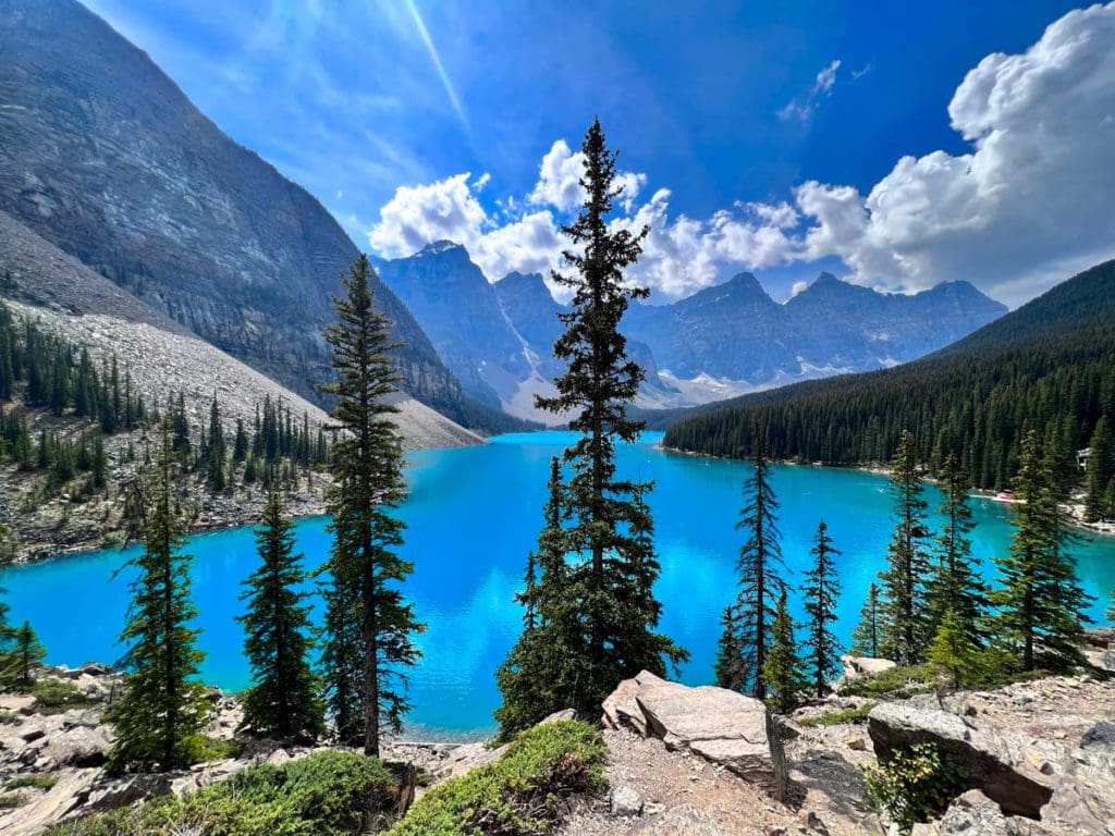 Moraine Lake with shimmering blue waters surrounding by mountain on a sunny day.