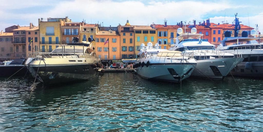Large boats rest along a dock with colorful buildings in the background along the shore of Cassis, visiting here is one of our tips for visiting the south of France with kids.
