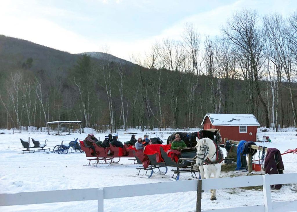People sit on horse-drawn sleighs, ready to depart for an evening ride in Stowe.