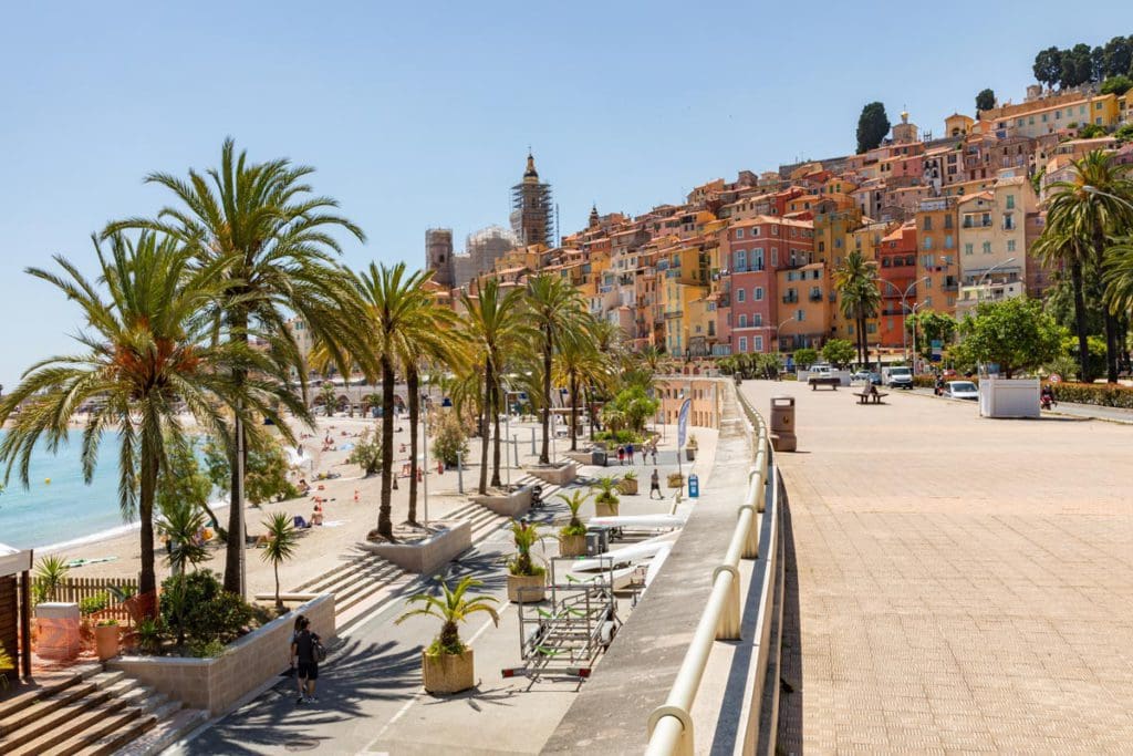 Palm trees flank the beach with the colorful homes of Nice in the distance.