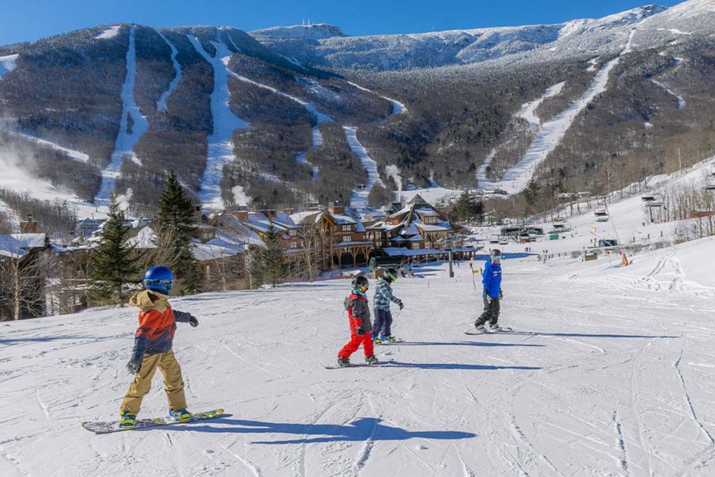 An instructor leads a few young skiers down a slope during ski school at Stowe Resort, one of the best places for lessons when skiing in Stowe with kids.