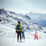 A mom and her two kids ski along a mountain trail in Italy.