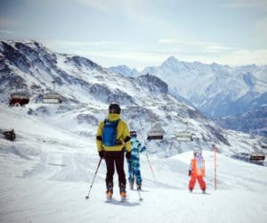 A mom and her two kids ski along a mountain trail in Italy.