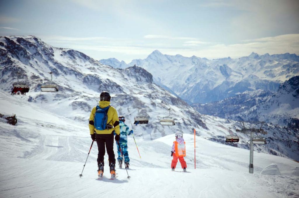 A mom and her two kids ski along a mountain trail in Italy, one of the best places to ski Europe with Kids.
