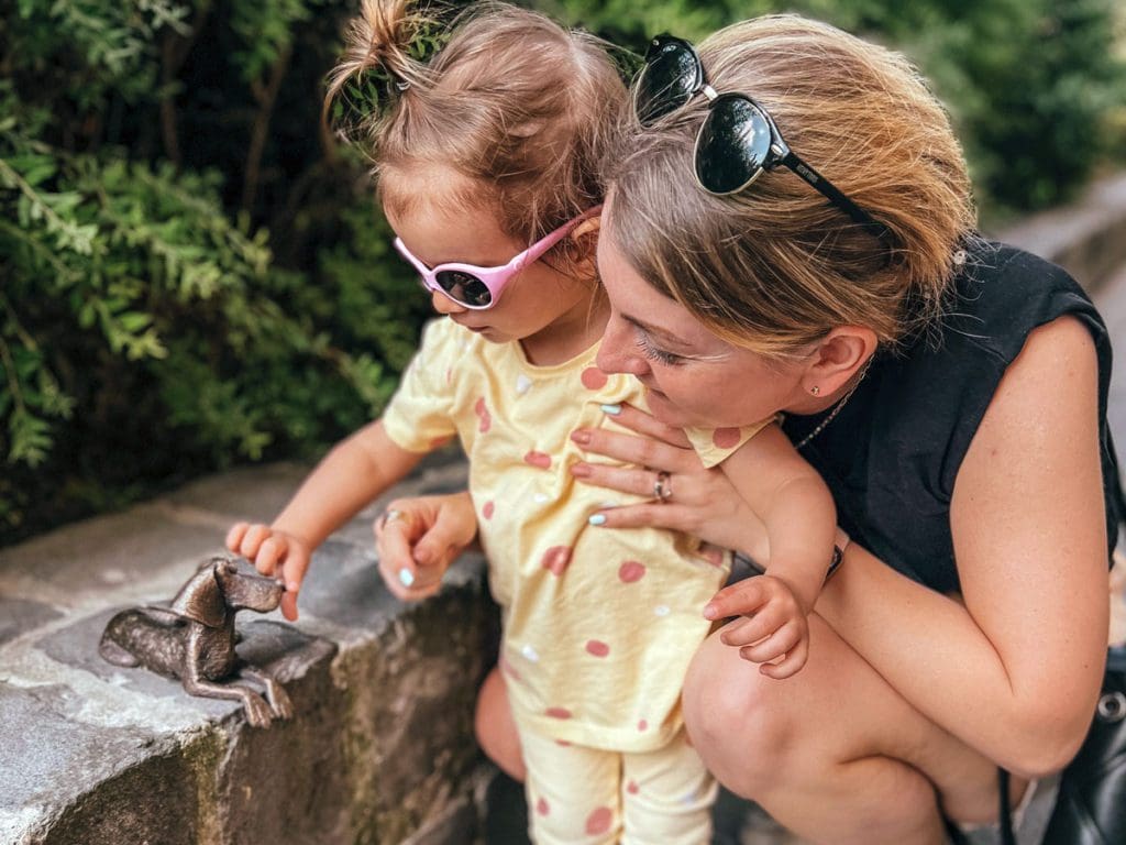 A mom holds her young toddler up to look at a tiny sculpture, as part of a tour in Budapest.