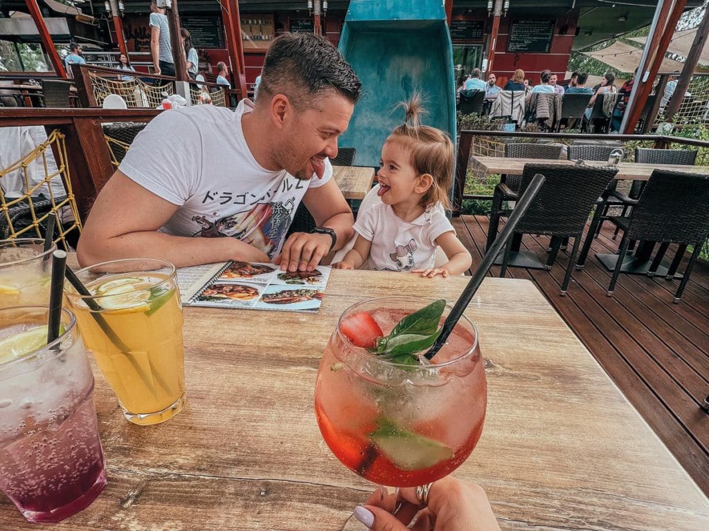A dad and his young daughter make silly faces at each other while dining at a restaurant in Budapest.