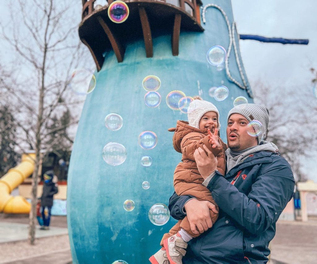 A dad holds his young daughter while they play with bubbles in a playground in Budapest.