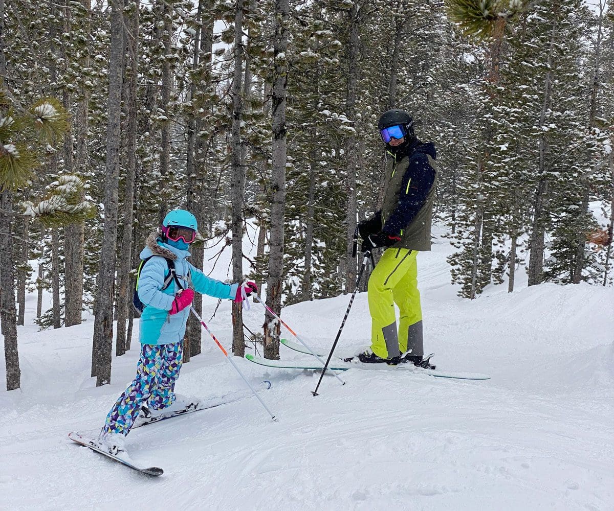 A dad and his young child stand on skis along an alpine run while skiing Big Sky with kids.