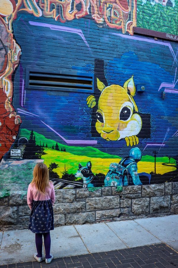 A young girl looks at a mural part of the Freak Alley Gallery in Boise, featuring a large yellow squirrel. 