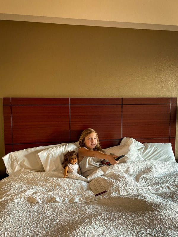 A young girl sits in bed with her doll at the Hampton Inn & Suites Boise-Downtown.