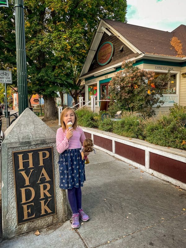 A young girl licks an ice cream while standing near a stone sign reading "Hyde Park".