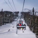 A ski lift holding a family of skiers moves up-mountain at Big Sky, one of the best ski resorts for families in the United States.