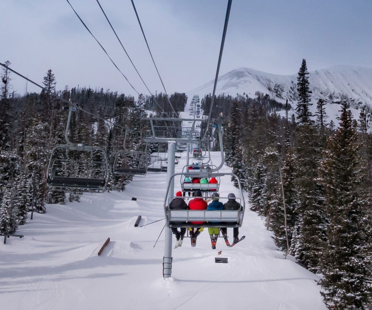 A ski lift holding a family of skiers moves up-mountain at Big Sky, one of the best ski resorts for families in the United States.