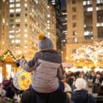 A young child sits atop the shoulder of an adult to take in a view of the lights and market sights at Christkindlmarket Chicago.