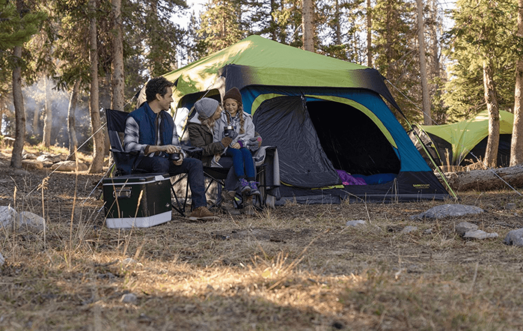 A family of three sits in front of the Coleman Cabin Tent, while enjoying a camping trip in the woods.