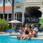 A family of four sits together laughing, while enjoying a poolside and sunny day at Curacao Marriott Beach Resort.