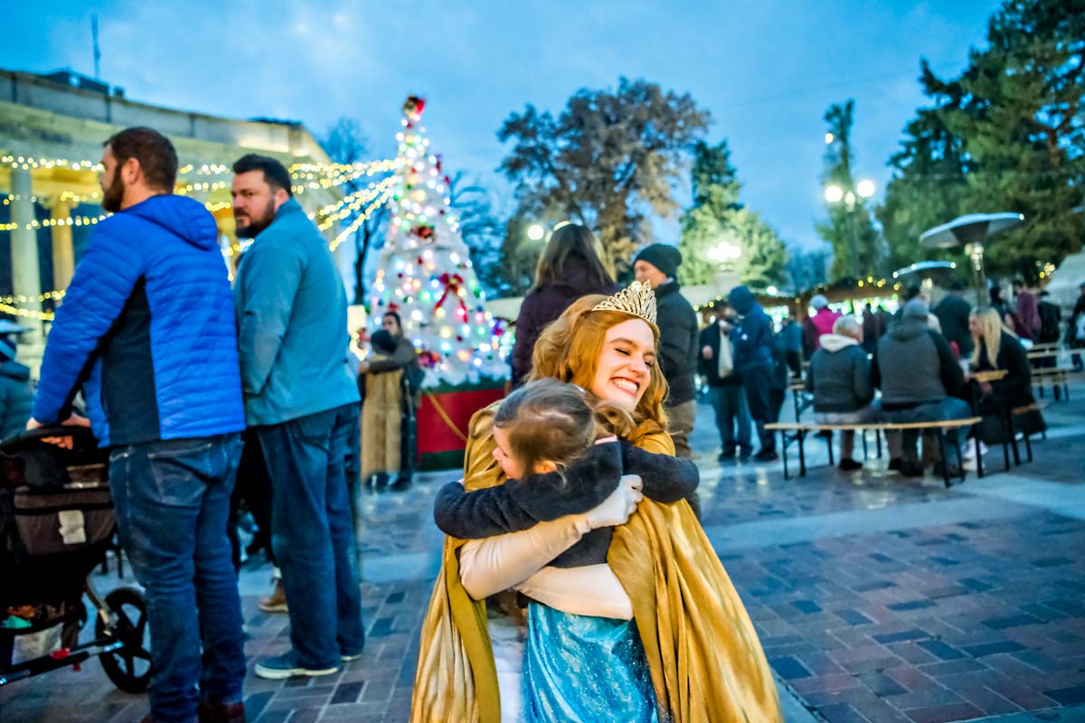 A young girl hugs a market princess at the Denver Christkindlmarket, one of the best christmas markets in the United States for families.