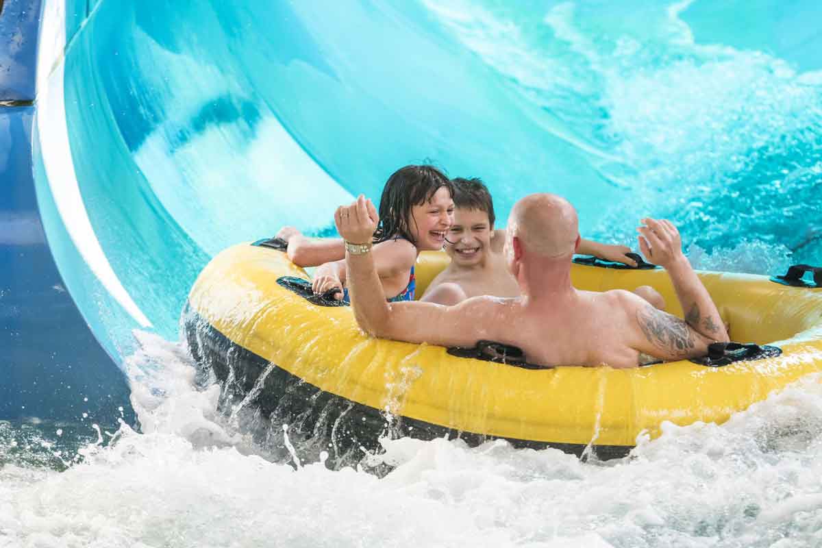 A dad and his two kids shoot down a waterslide on a large yellow tube at Great Wolf Lodge Williamsburg. 