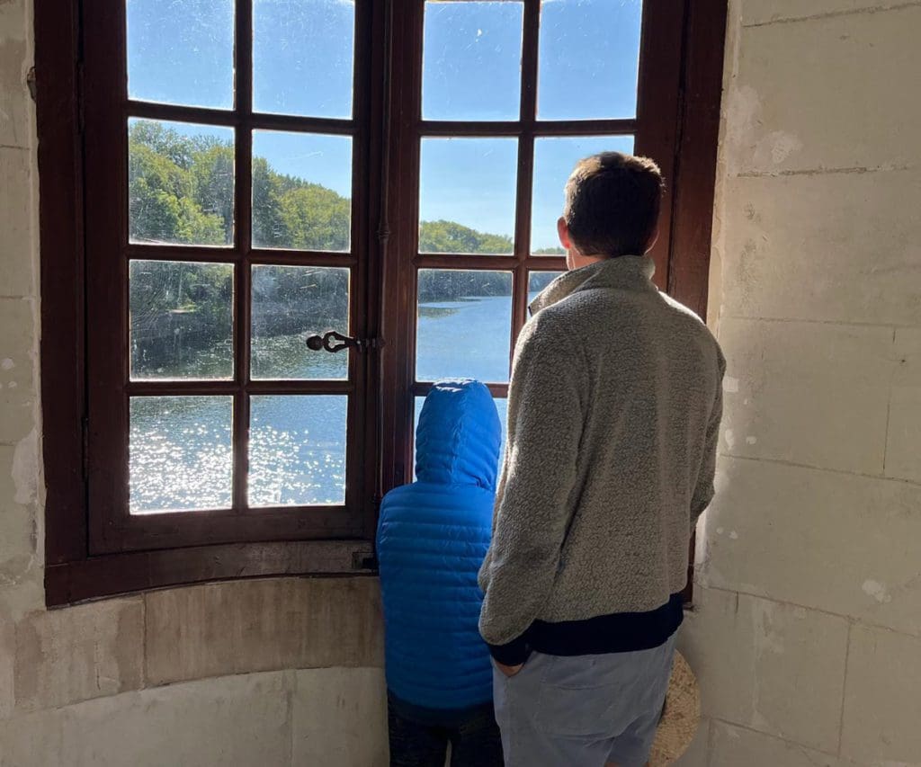 A dad and his young son look out the window of a chateau in France.