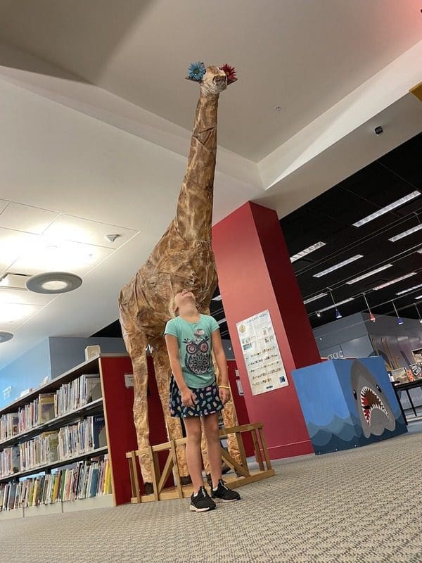 A teen looks up at a giraffe inside the Greenville Library.