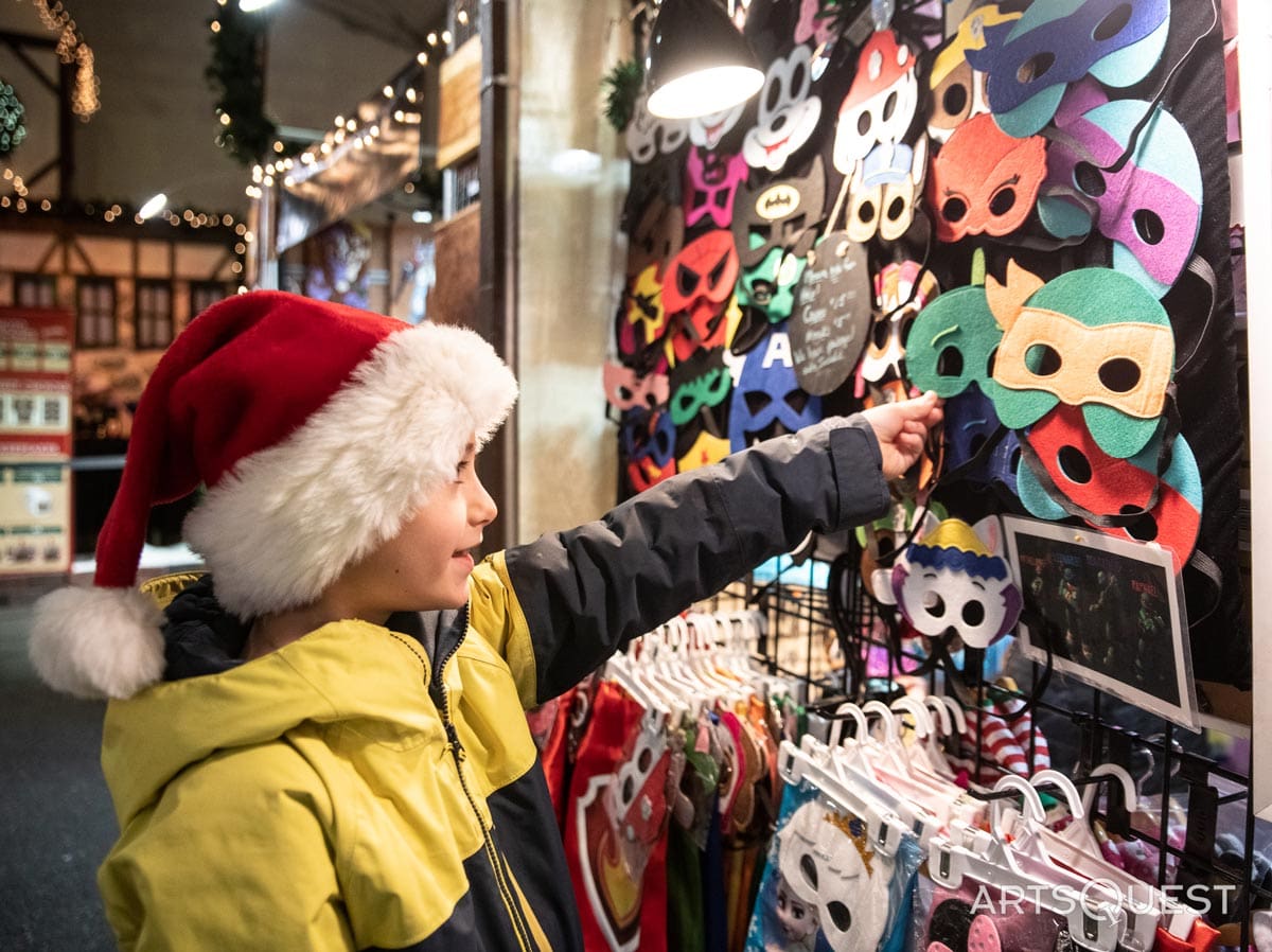 A small child points at a row of masks for sale at a vendor at Christkindlmarkt Bethlehem.