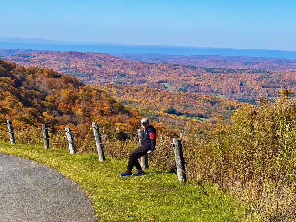 A young boy sits along a fence with an expansive view of colorful fall foliage in the distance at Pittsfield State Forest.