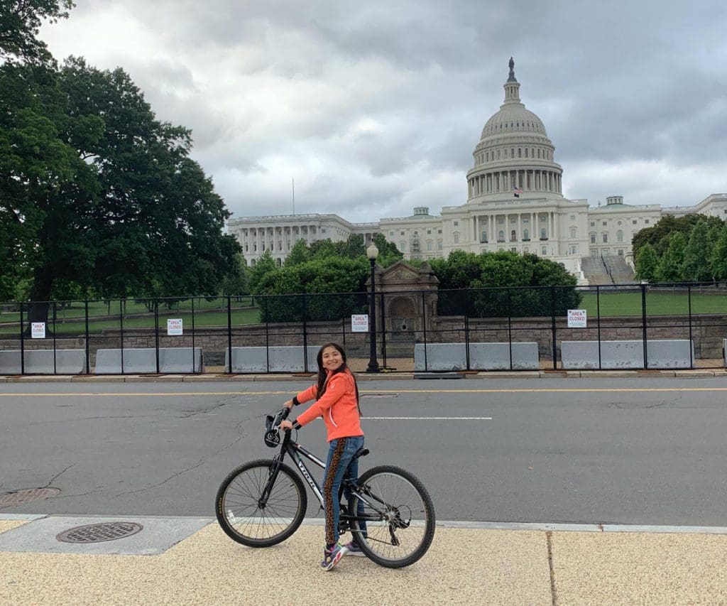 A tween girl rides a bike in front of the US capitol building while exploring Washington DC.