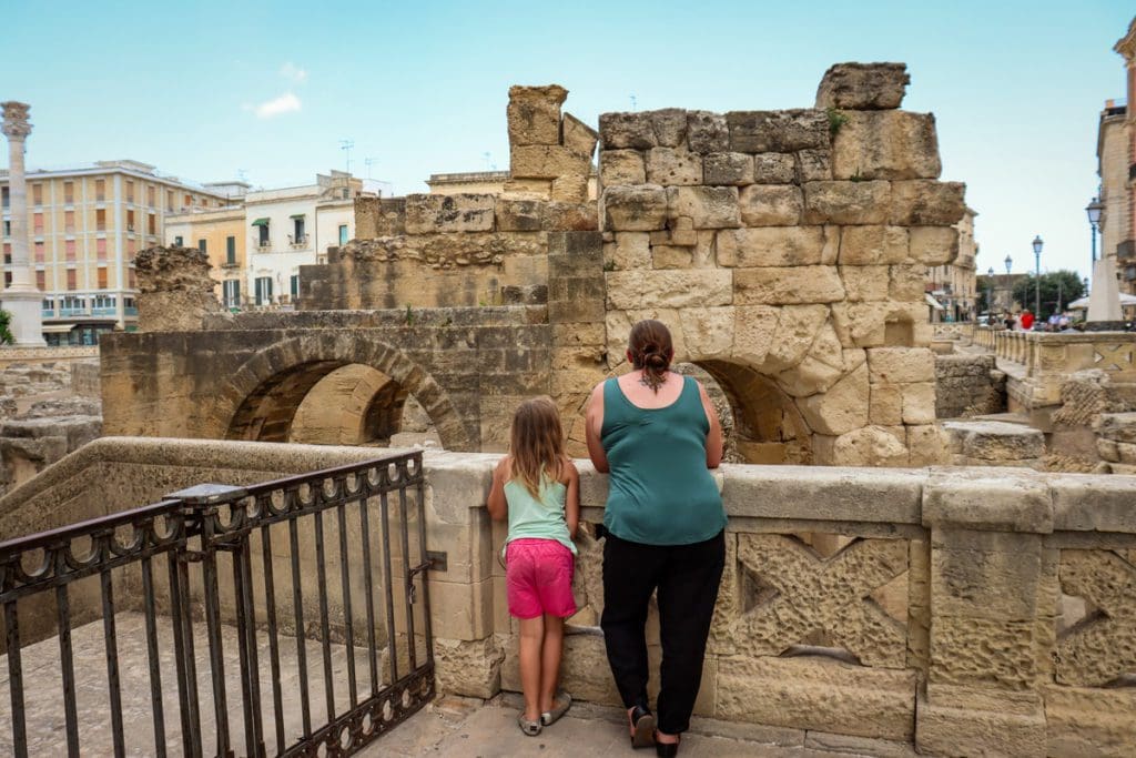 A mom and her young daughter stand together looking at Roman ruins in Lecce, one of the best places to visit in Puglia with kids.