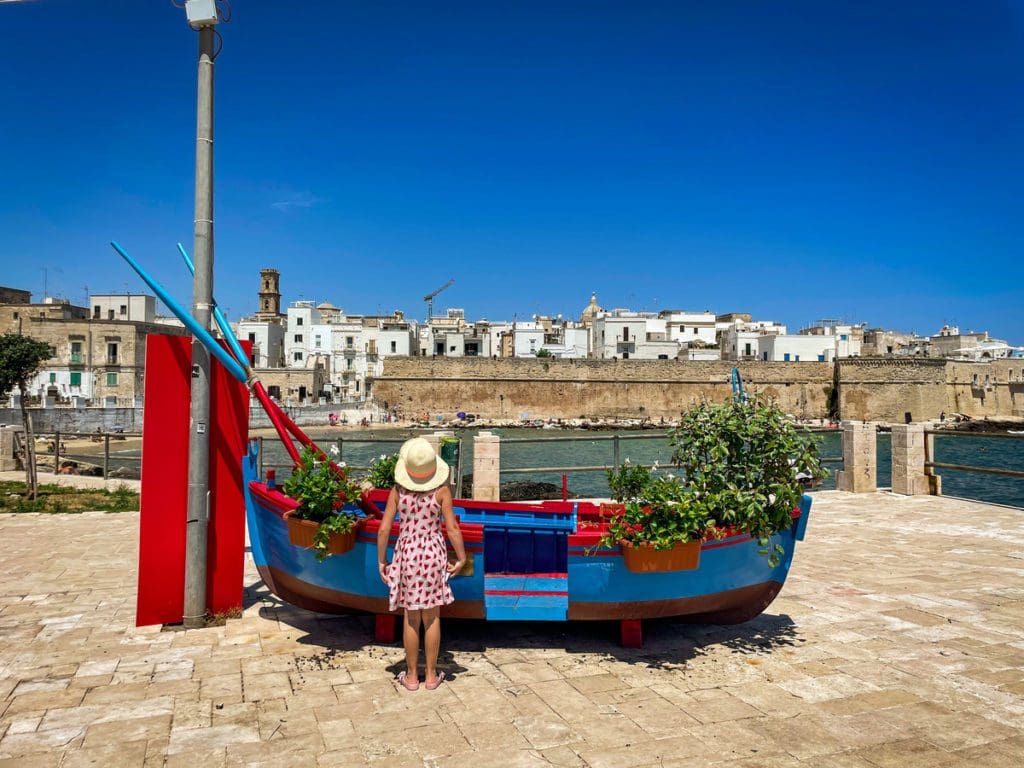 A young girl stands near an example of a traditional fishing boat in Monopoli, one of the best places to visit in Puglia with kids.