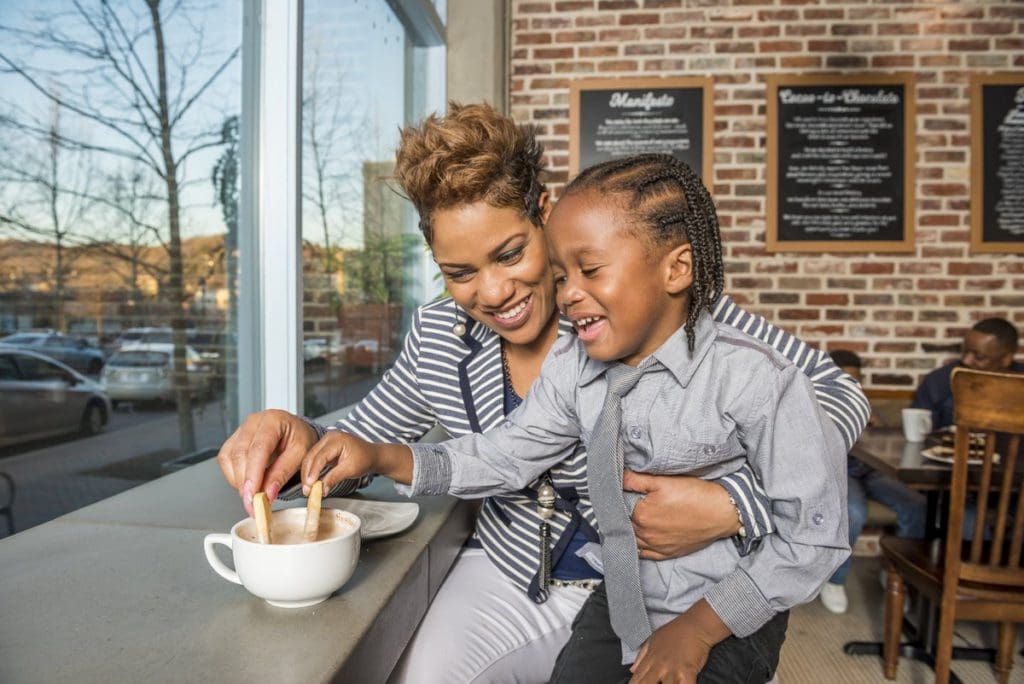 A mom of color and her young son dip biscotti in a mug of hot chocolate at a cafe in Downtown Asheville.
