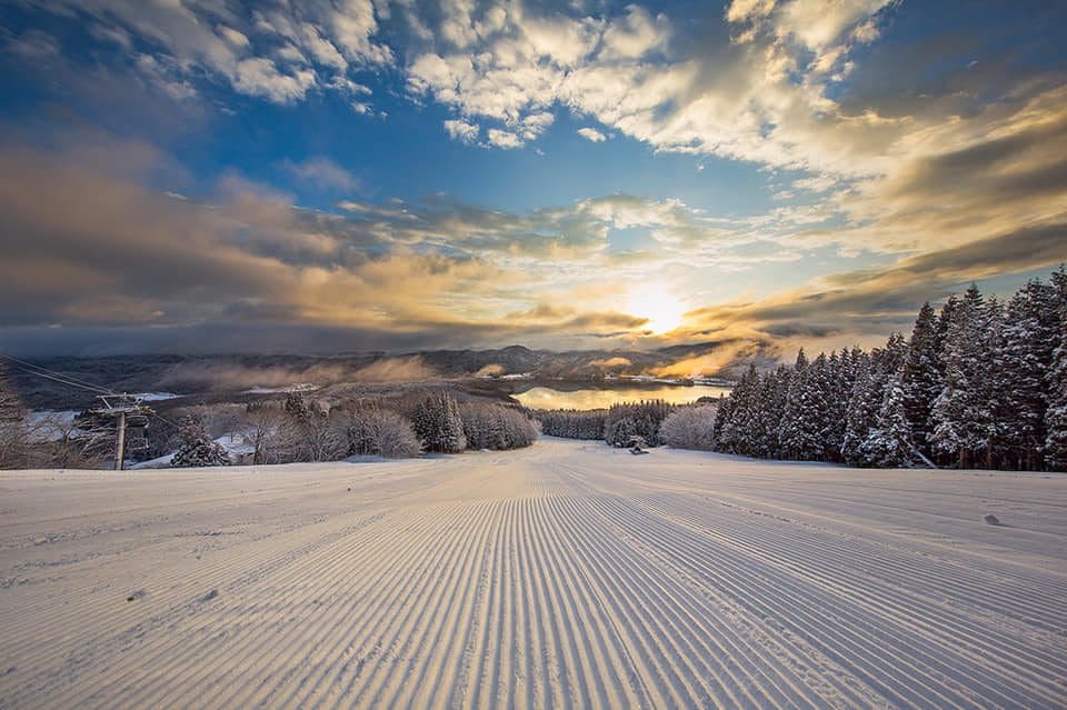 A ski run goes along Hakuba Valley toward the ski, which is brightly lit with a sunset.