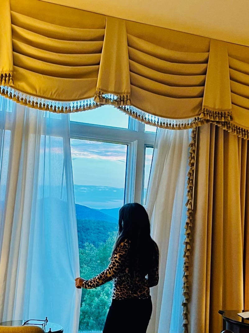 A woman pulls back the drapes to take in mountain views form a hotel room at Inn at Biltmore, a great stay on this Asheville family vacation itinerary.