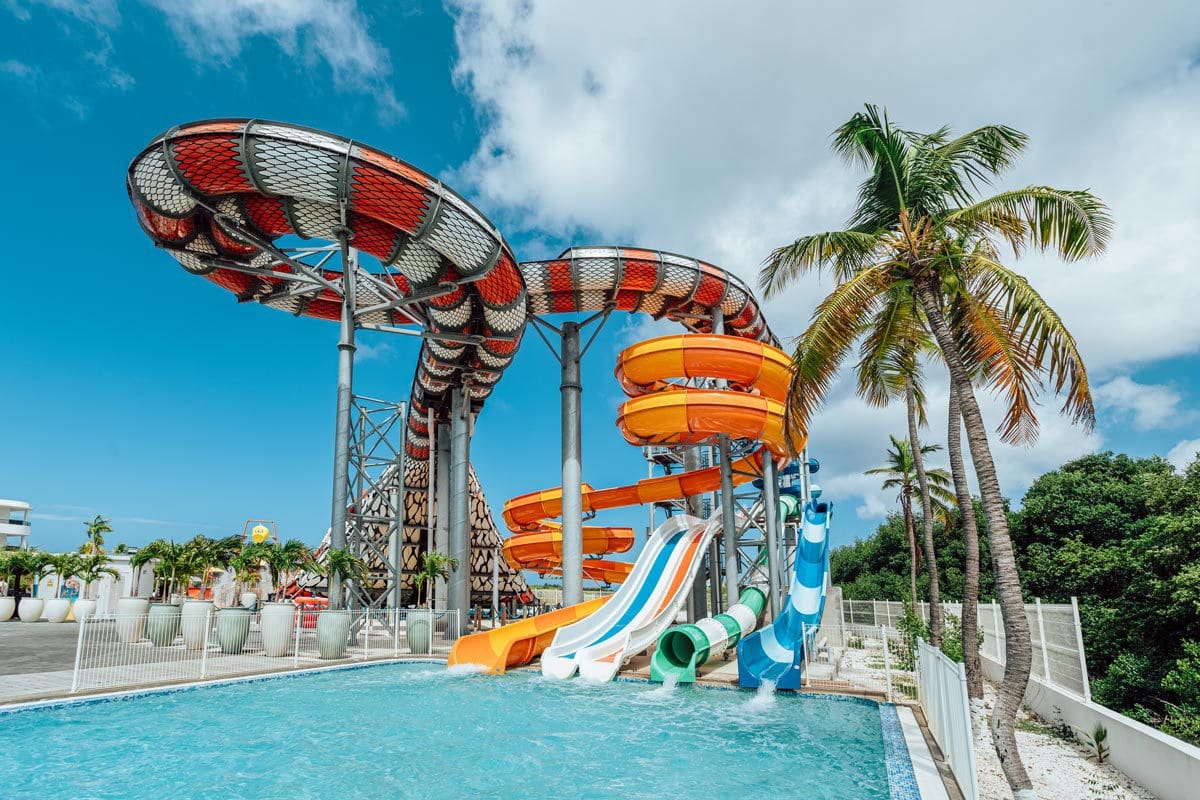 A large waterslide shoots into a pool at the Mangrove Beach Corendon Curacao All-Inclusive Resort, Curio Collection.