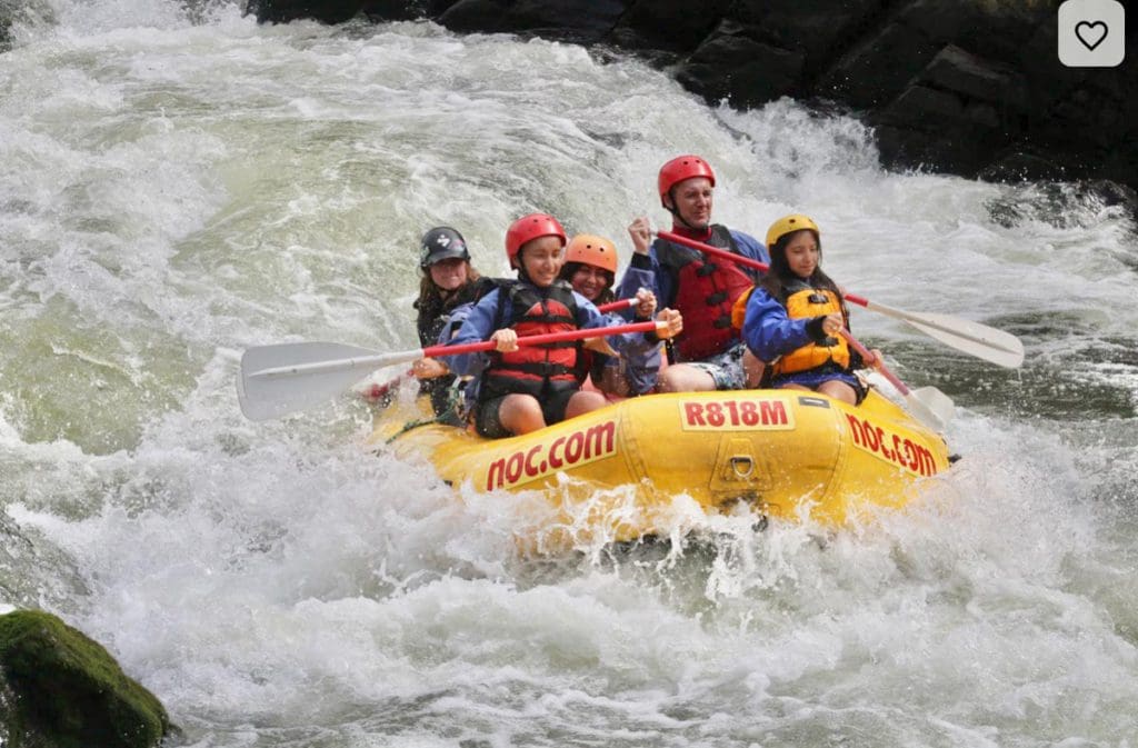A family white water rafts down a river together, a must do with older kids and teens on any Asheville family vacation itinerary.