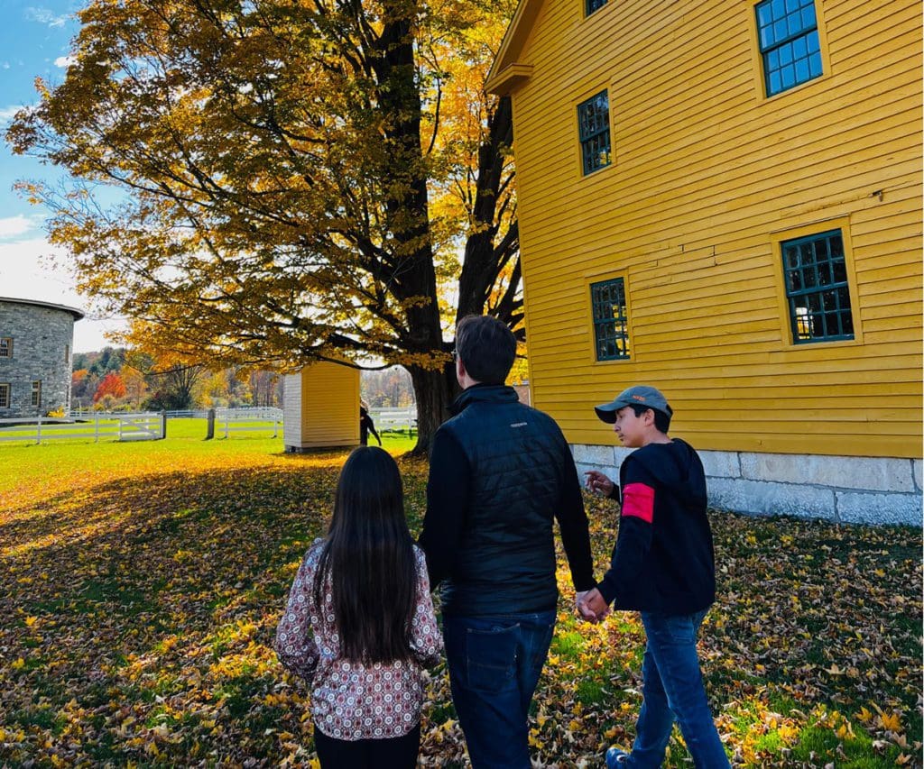 A dad walks hand in hand with his two kids as they walk across the lawn near some of the buildings at Hancock Shaker Village.
