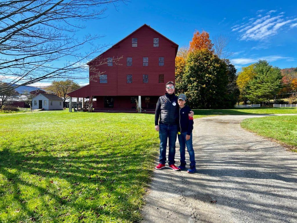 A dad and his son stand together outside a red building at Hancock Shaker Village, near Pittsfield, MA.