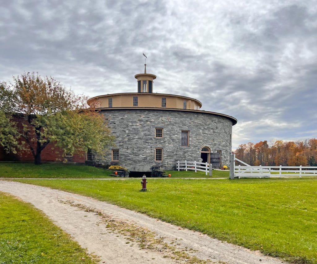 The Round Stone Barn across the lawn at Hancock Shakers Village on a cloudy, fall day.