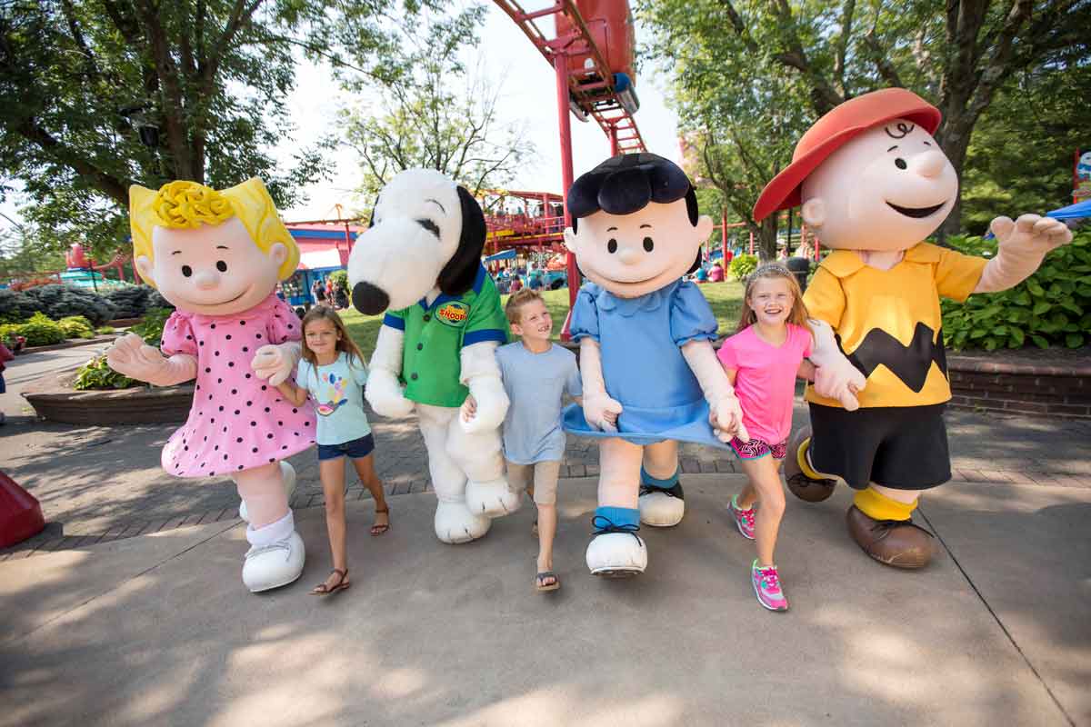 Three kids walk hand-in-hand with Snoopy characters at Kings Dominion, including Lucy and Charlie Brown.
